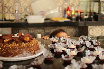 Close-up of child behind cakes on kitchen counter 