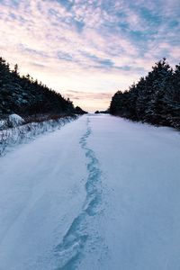 Snow covered field against sky during sunset