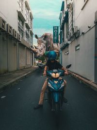 Woman riding motorcycle on road amidst buildings in city