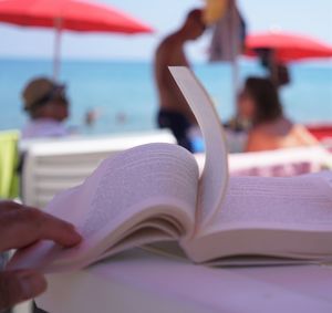 Cropped hand of person holding book page on table at beach