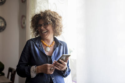 Laughing woman holding phablet by the window