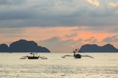 Silhouette boats in calm sea at sunset
