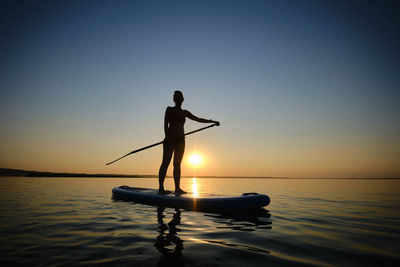 Silhouette man standing in sea against sky during sunset