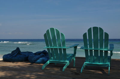 Adirondack chairs with bean bags on pier against sky