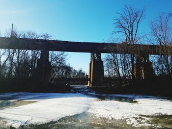 Bridge over frozen river against sky during winter