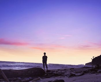 Man standing on rock by sea against sky during sunset