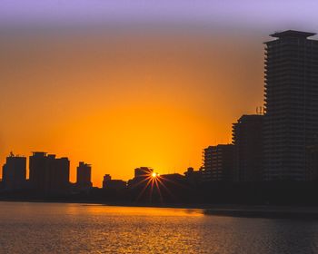 Buildings by river against sky during sunset