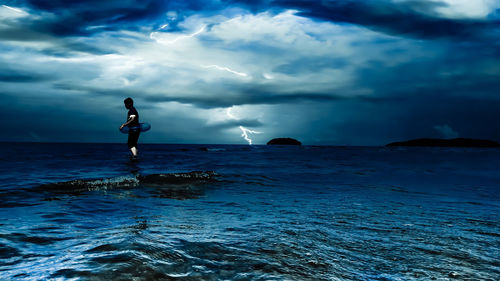 Side view of boy with inflatable ring in sea against thunderstorm cloudy sky