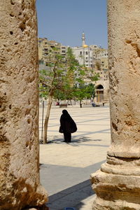 Veiled woman walking by historical building in city against clear sky