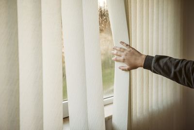 Cropped hand of man standing by window