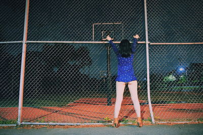 Rear view of woman standing by chainlink fence