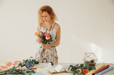 Florist arranging flowers while standing at table against white background