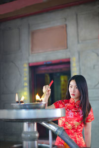 Young woman burning incense while standing against built structure