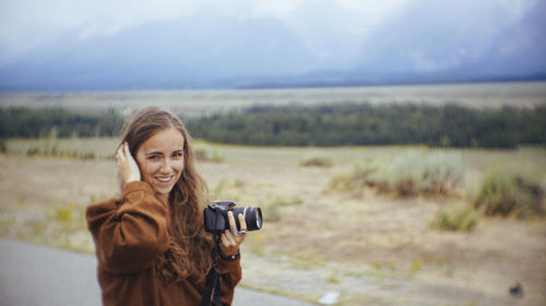 Portrait of smiling woman standing on field against sky