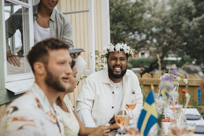 Portrait of happy young man wearing tiara while sitting with friends during dinner party at cafe