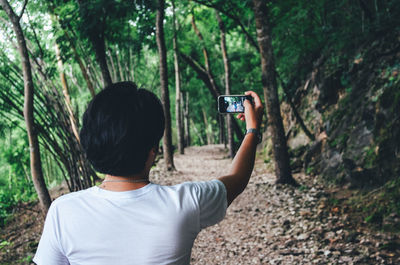 Rear view of man taking selfie while standing on footpath in forest