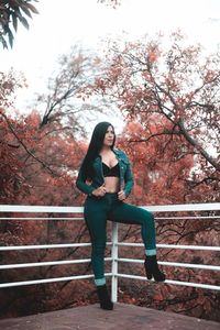 Full length portrait of woman sitting against trees