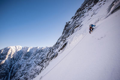 Alpine climber ascending steep snow with mountains behind