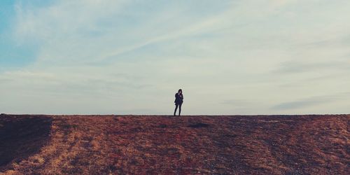 Mid distance view of young woman standing on field against sky