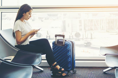 Young woman using phone while sitting on seat at airport