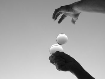 Low angle view of person balancing crystal balls against clear sky