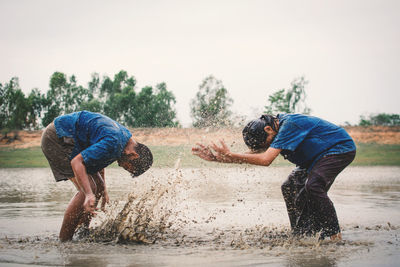 Siblings playing in lake against sky