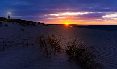 Scenic view of beach against cloudy sky during sunset