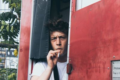 Portrait of young man smoking cigarette while standing at doorway