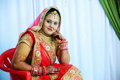 Portrait of bride sitting on chair against white curtain