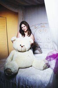 Portrait of young women with large teddy bear on bed