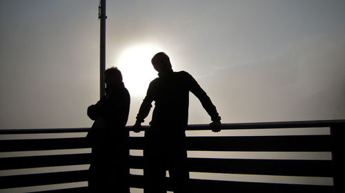 Silhouette of people on railing against sky