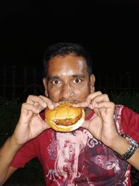 Portrait of man eating ice cream against black background