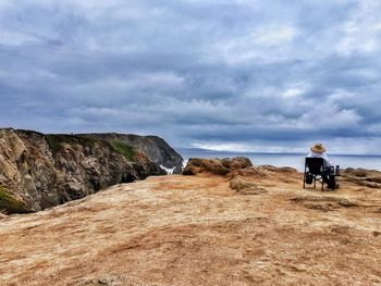 Lone man in straw hat sitting whale watching against ocean and cloudy blue sky background.