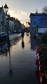 Man walking on wet road against sky in city