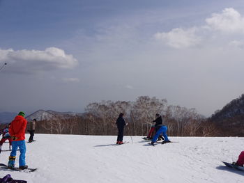 People skiing on field against sky during winter