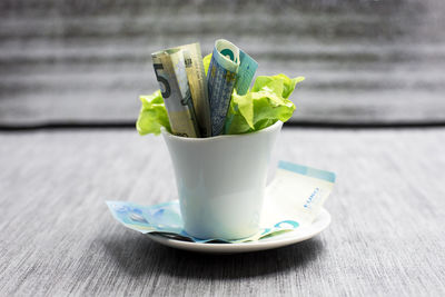 Close-up of paper currencies in cup on plate over table