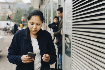 Mid adult woman using mobile phone while walking on sidewalk in city