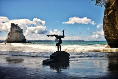 Man standing on rocks by sea against sky