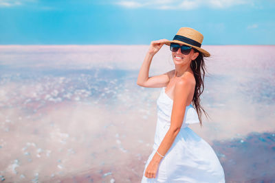 Woman wearing hat standing at beach against sky
