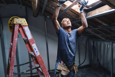 Mature construction worker repairing ceiling in attic