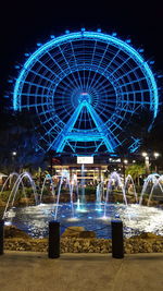 Illuminated ferris wheel against blue sky at night