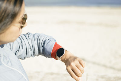 Closed side view, latina woman with sunglasses looking at smart watch, light background