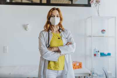 Confident female doctor wearing protective face mask standing with arms crossed at clinic