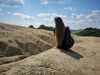 Woman with long hair sitting on rock against sky