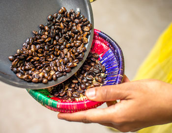 Cropped hands of woman pouring roasted coffee beans in container from frying pan