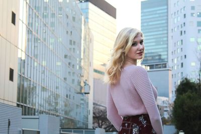 Portrait of young woman standing against buildings in city