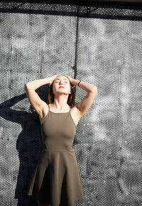 Thoughtful young woman with eyes closed while standing against warehouse