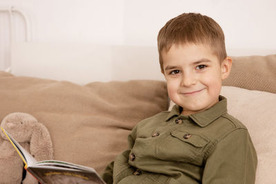 Little and cute caucasian boy reading a book on the bed at home. 