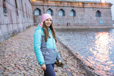 Happy tourist woman on the bank of the river in autumn in warm clothes.