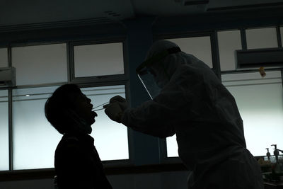 Side view of man standing against window doing swab test for corona virus